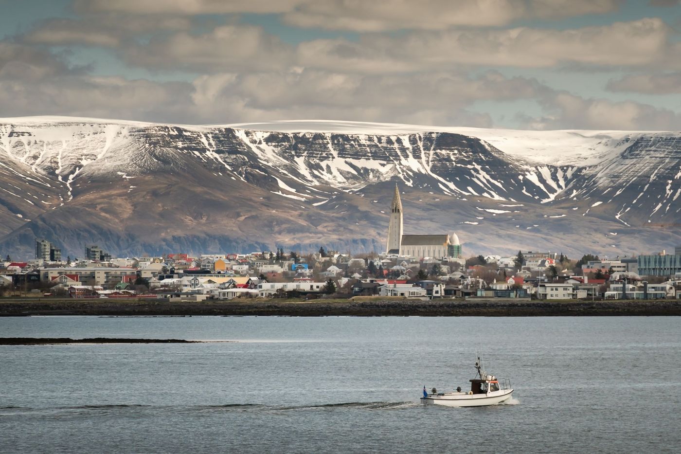 A small boat heading out across the bay, with Reykjavik and Hallgrímskirkja behind it