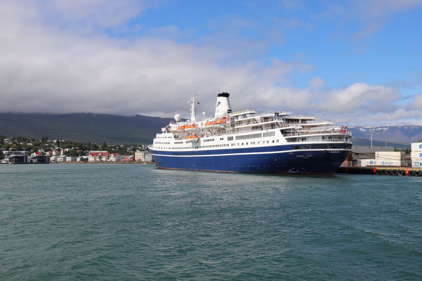 A white and blue cruise ship docked at Akureyri harbour, mountains behind