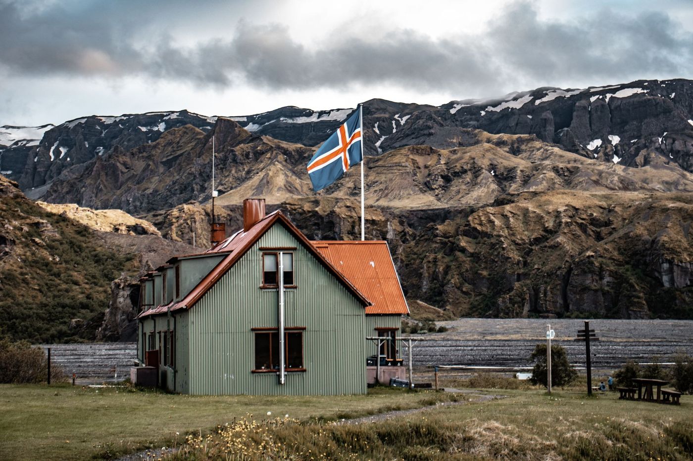 A red-roofed house flying the Icelandic flag below dark mountains