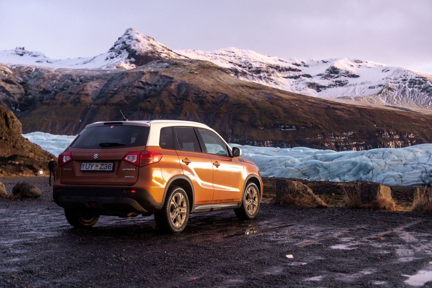 Un petit SUV orange garé sur du gravier au pied d'un glacier en Islande