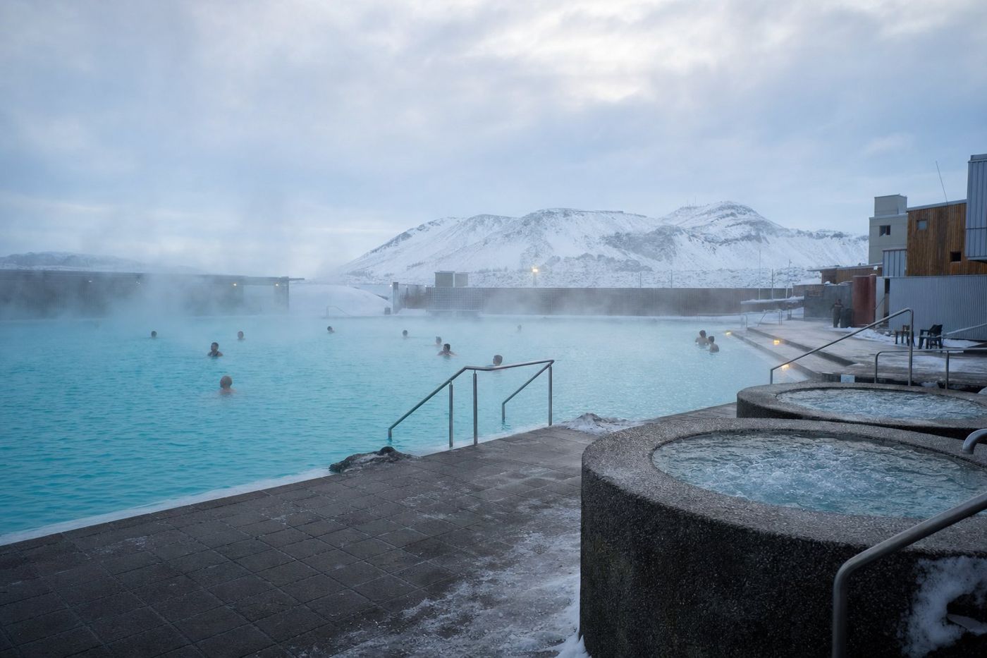 De la vapeur s'élevant d'un bassin géothermique en plein air par temps froid, avec de la neige au sol