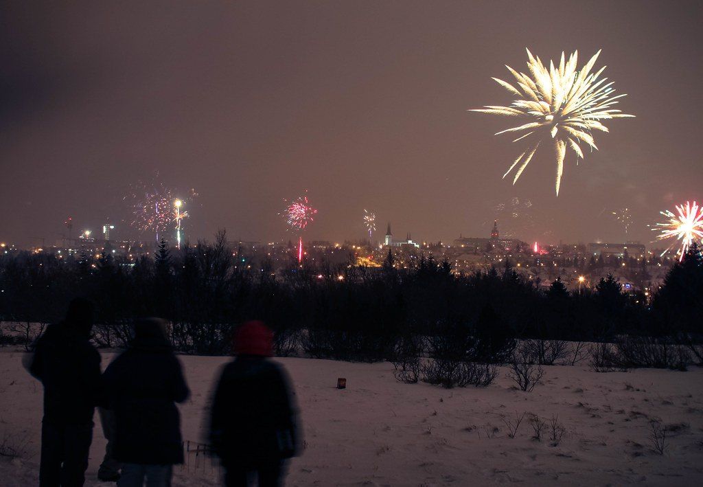 Feux d'artifice au-dessus de Reykjavik à minuit le soir du Nouvel An, des gens les regardent depuis une colline enneigée