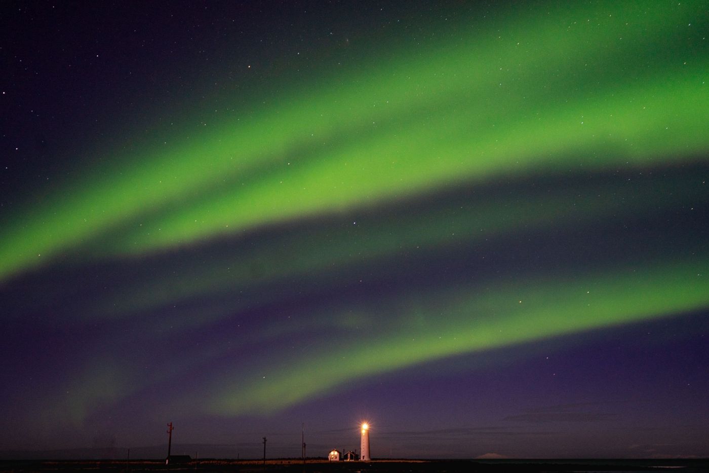 Aurore verte au-dessus de la mer, avec la lumière du phare de Grótta à l'horizon